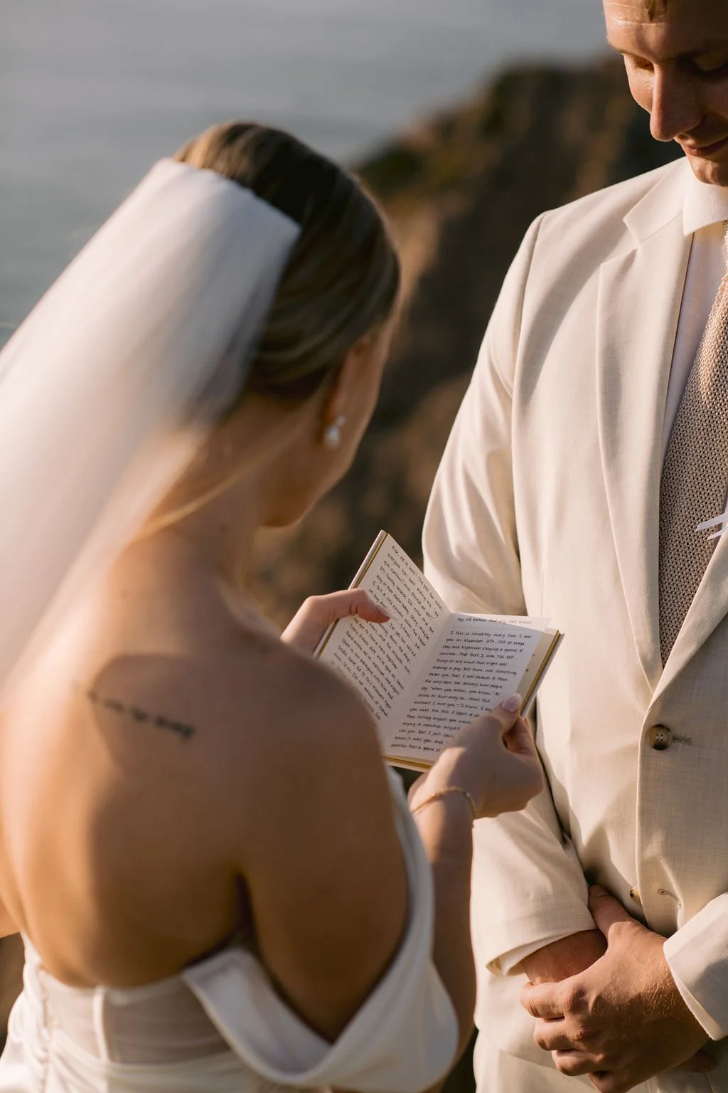 Elopement portrait of a bride and groom exchanging vows outdoors during their wedding ceremony, with the bride reading her vows from a small book.