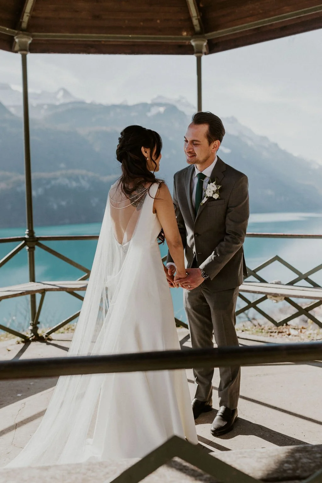 A bride and groom holding hands during their wedding ceremony outdoors with a mountain and lake backdrop.