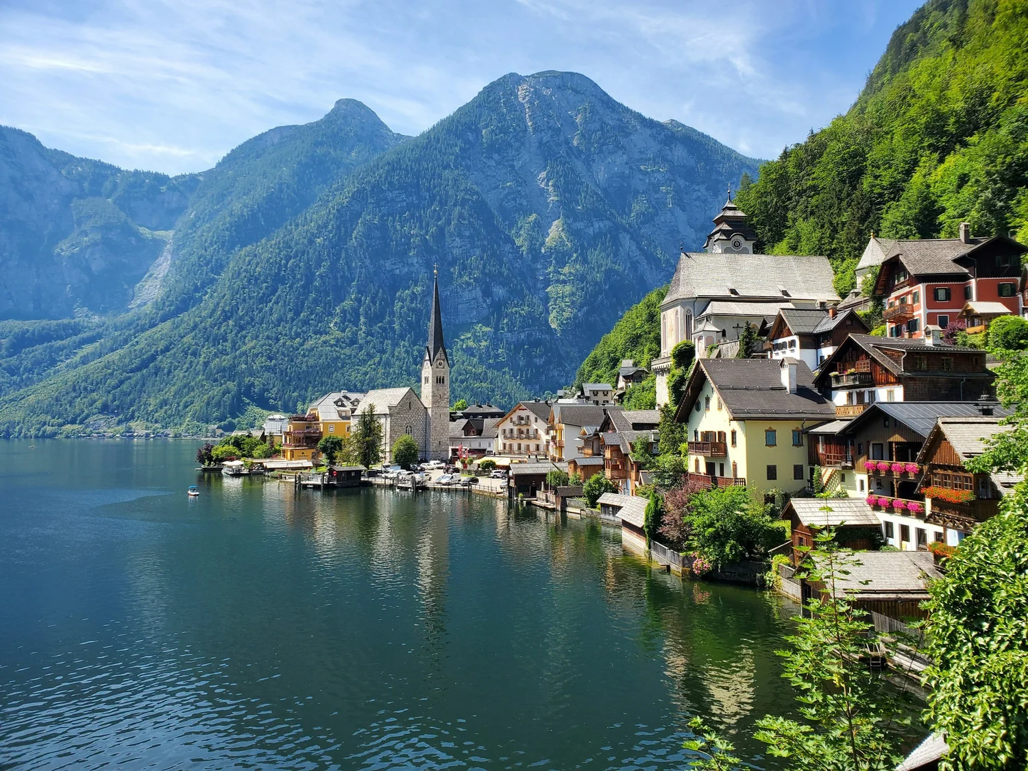 A scenic lakeside village with colorful houses and a church, surrounded by lush green mountains and clear blue sky.