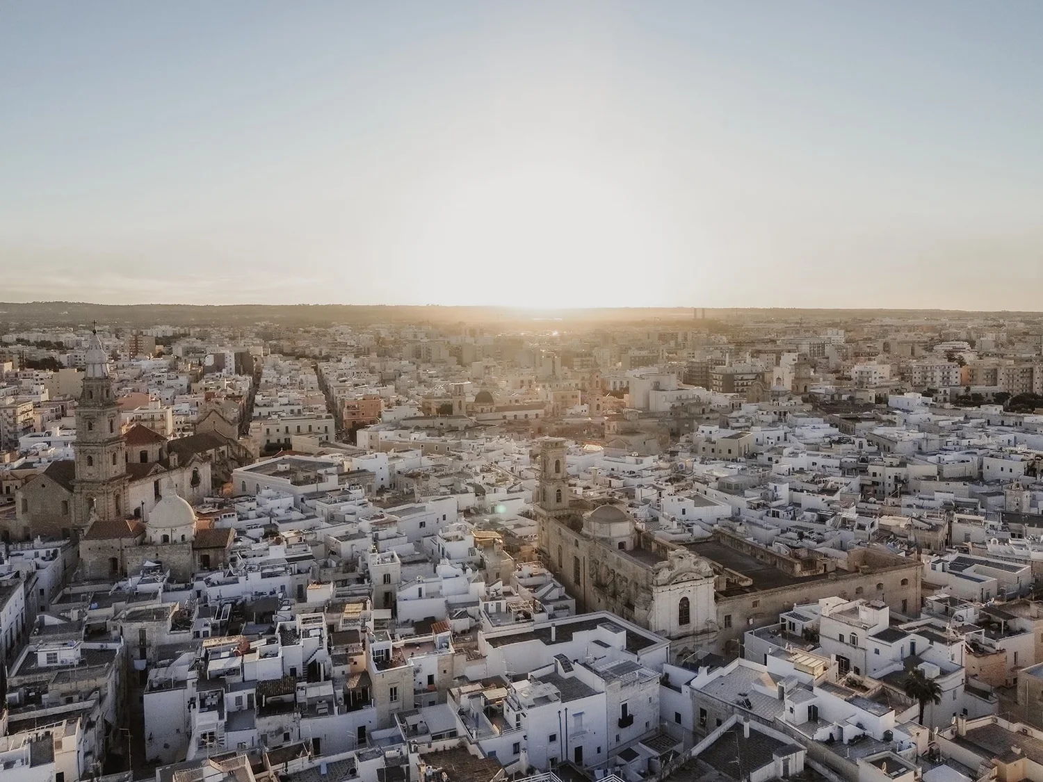 A panoramic view of a cityscape at sunrise with many white buildings, church towers, and a clear sky.