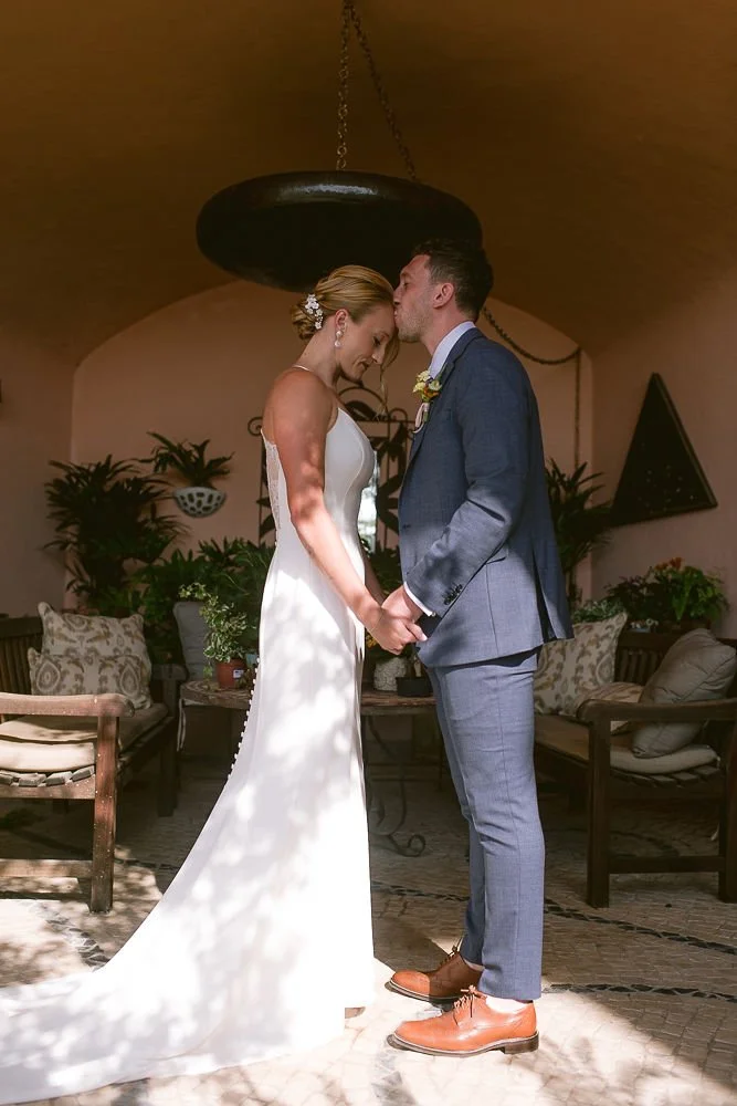 Bride and groom holding hands with foreheads touching in a cozy, well-decorated indoor setting during a wedding ceremony.