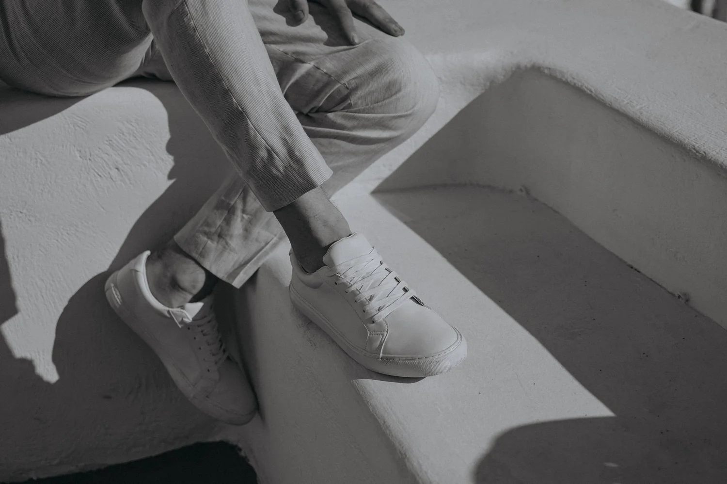 Close-up of a person sitting on a concrete ledge, wearing light-colored cargo pants and white sneakers.