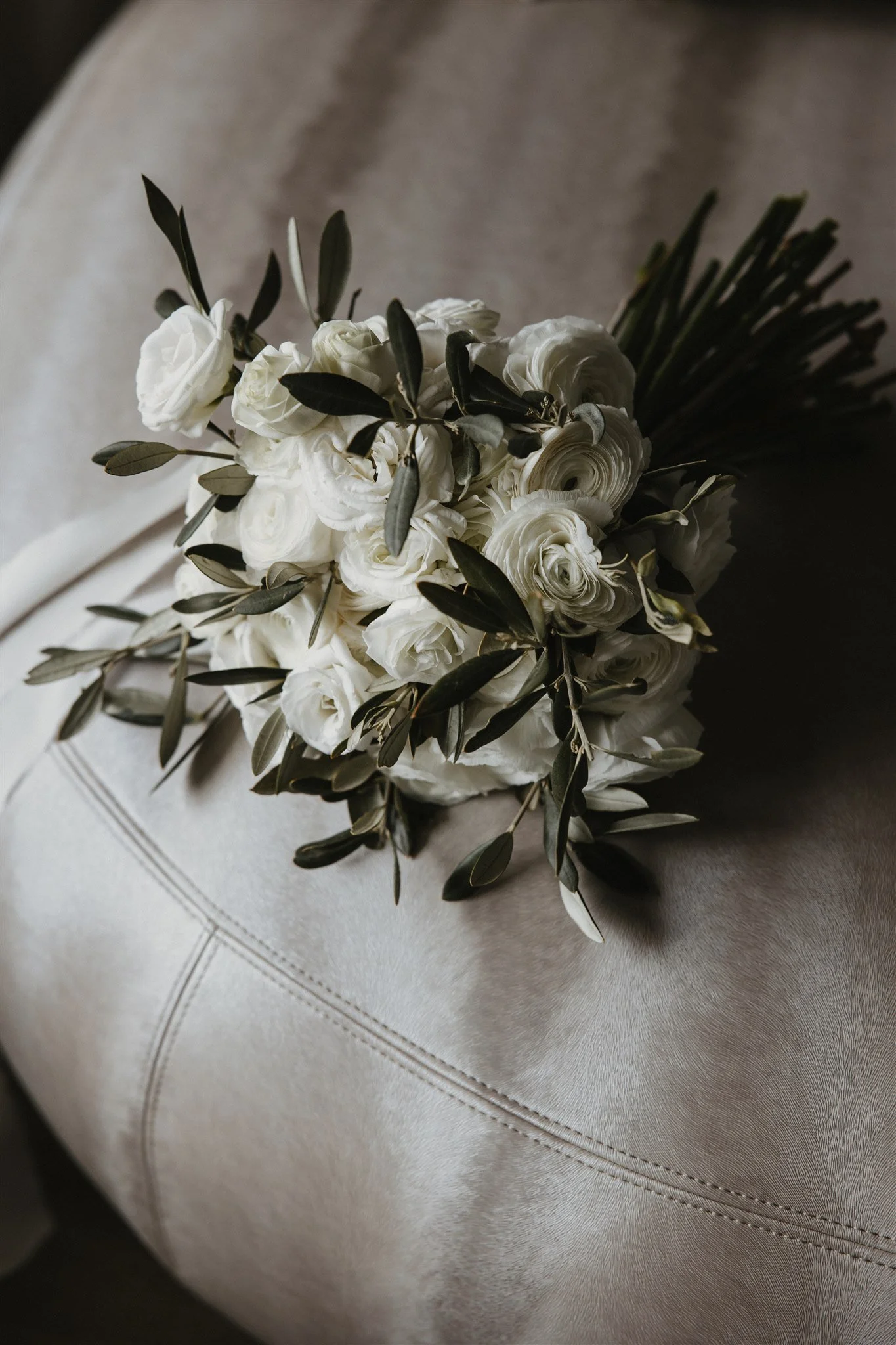 A bouquet of white roses and greenery resting on a light-colored fabric surface.