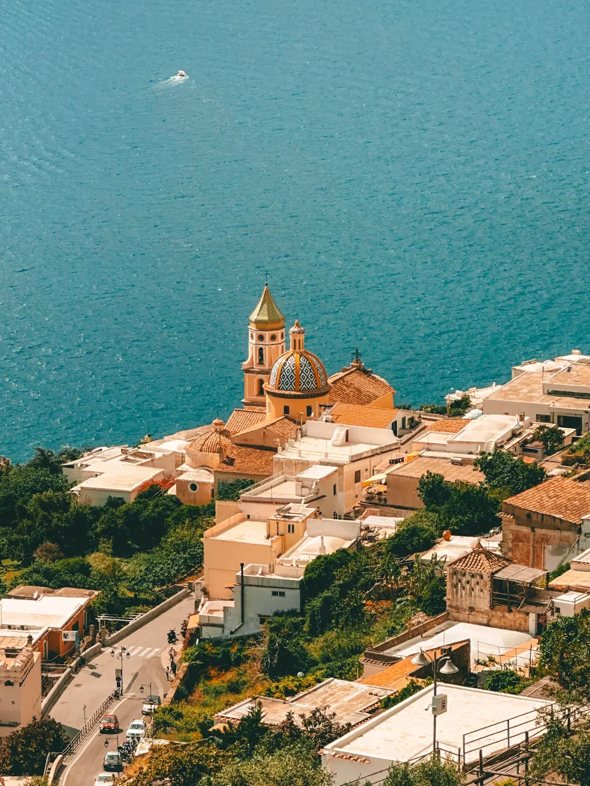 Town with colorful buildings and a church with a tiled dome, set against the blue sea, in a coastal area.