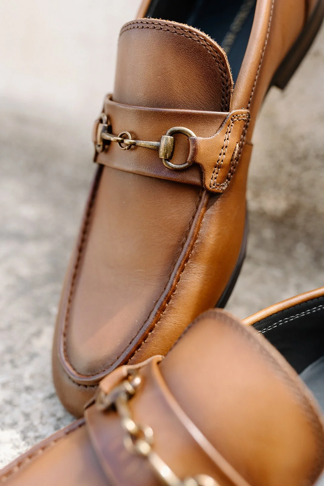 Close-up of a tan leather dress shoe with detailed stitching and a decorative metal bit across the vamp.