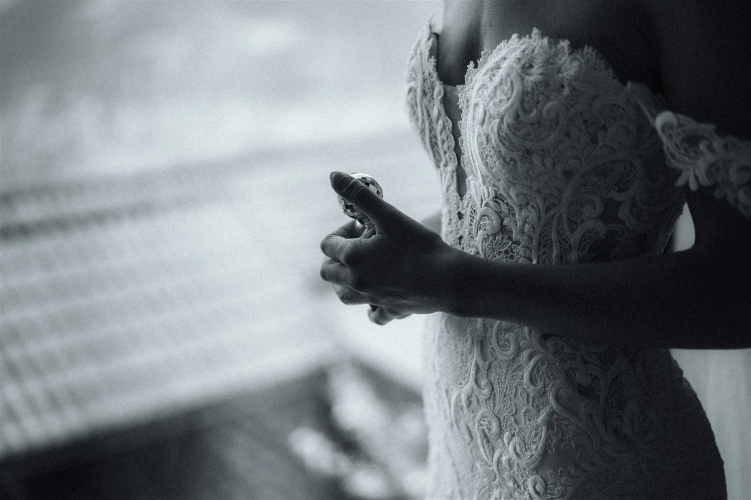 A close-up of a person's hand holding a poker chip, with part of their lace dress visible, set against a soft, blurry background.