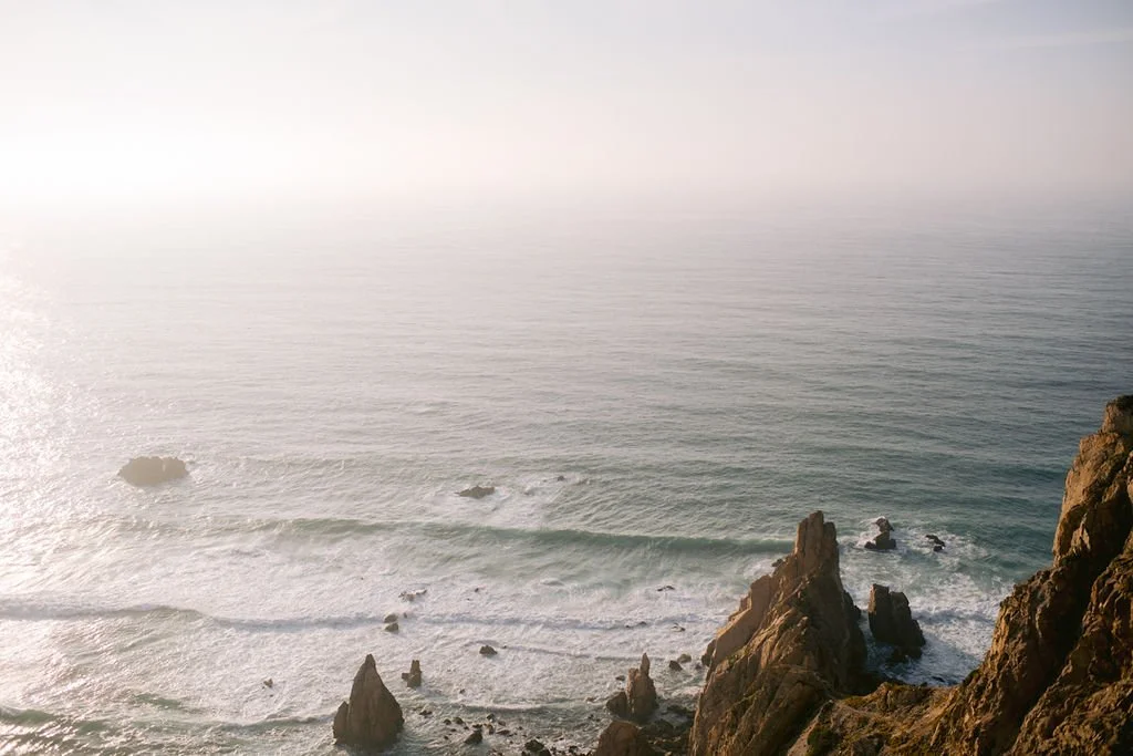 Ocean with waves breaking near rocky cliffs on the right side of the image.