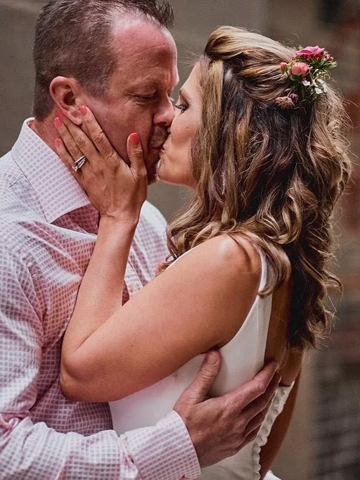 A couple sharing a kiss, with the woman holding the man's face and the man holding her waist, during a wedding or romantic moment.