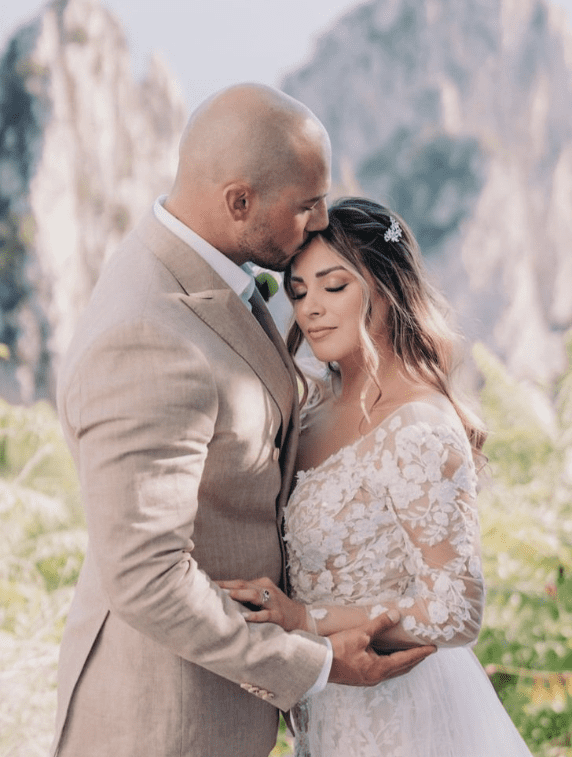 A couple in wedding attire sharing an intimate moment outdoors with mountains in the background.
