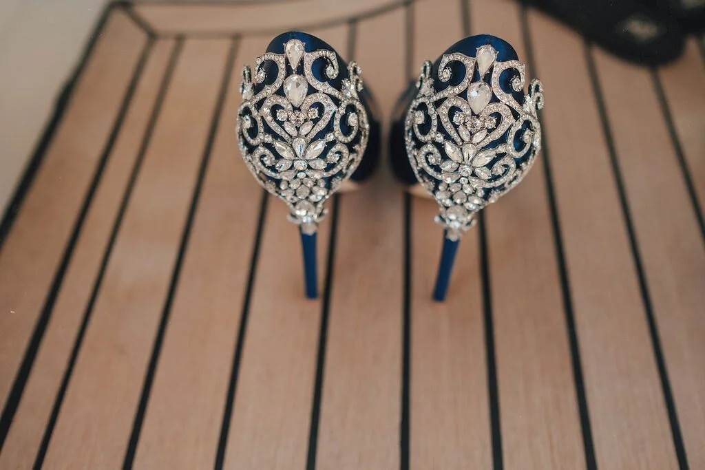 A pair of elegant high-heeled shoes decorated with intricate silver and rhinestone patterns, placed on a wooden surface.
