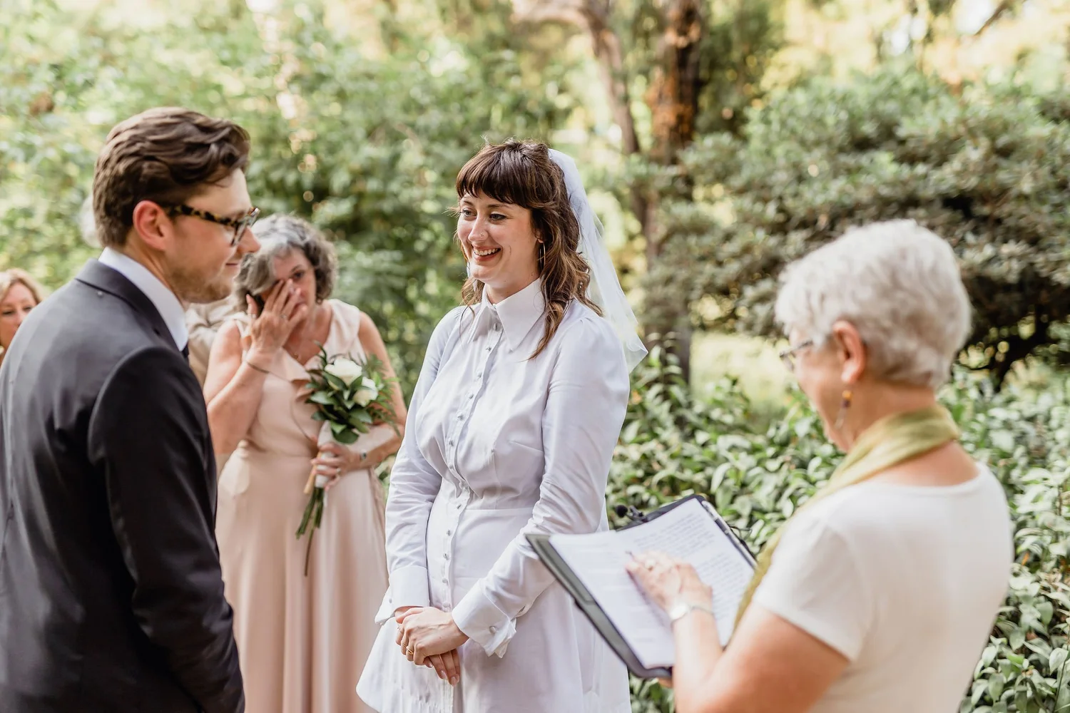 Couple exchanging vows during outdoor wedding ceremony with guests and officiant present.