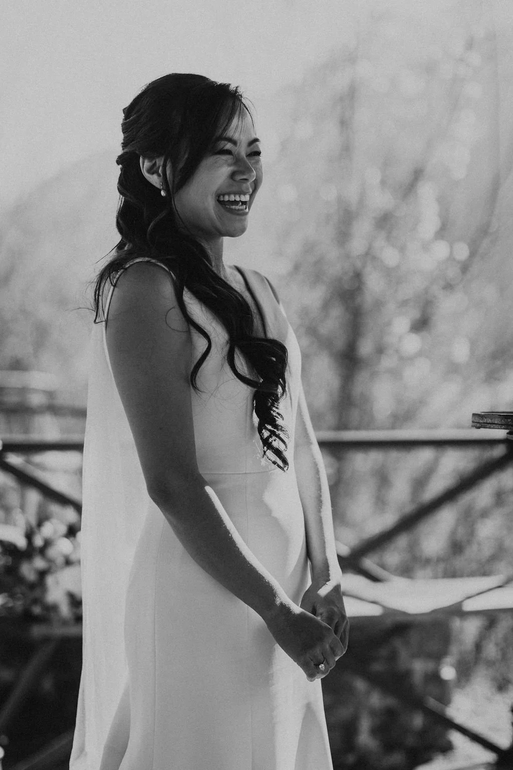A woman in a wedding dress is smiling and laughing outdoors.
