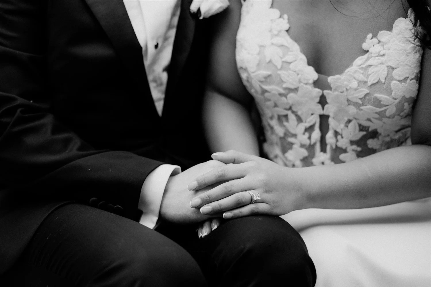 Close-up of a couple holding hands, with the bride wearing a wedding dress and the groom in a suit, during their wedding ceremony.