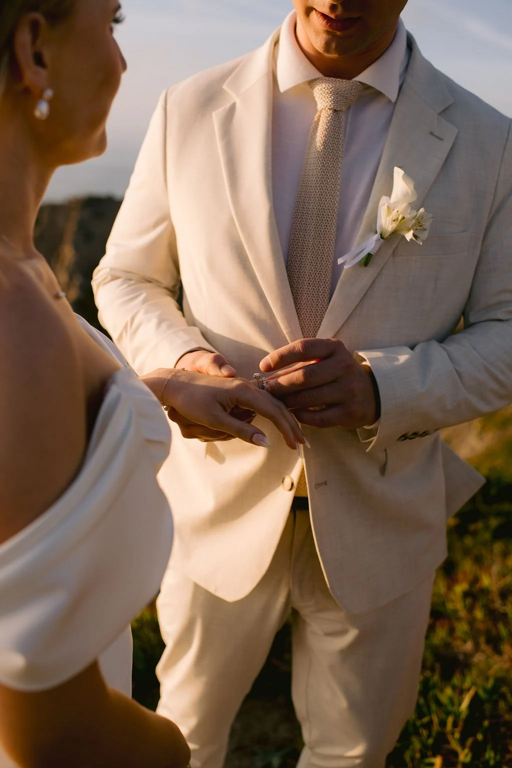 A couple exchanging wedding rings on a beach during sunset.