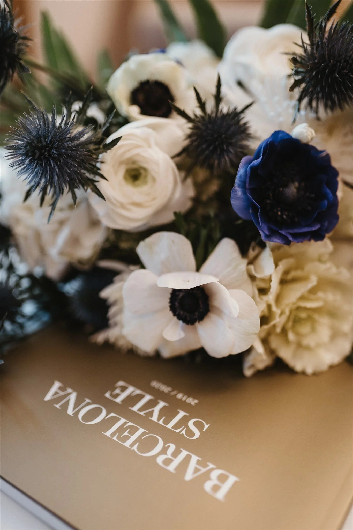 Close-up of a bouquet of white and dark purple flowers on a brown box with white text.
