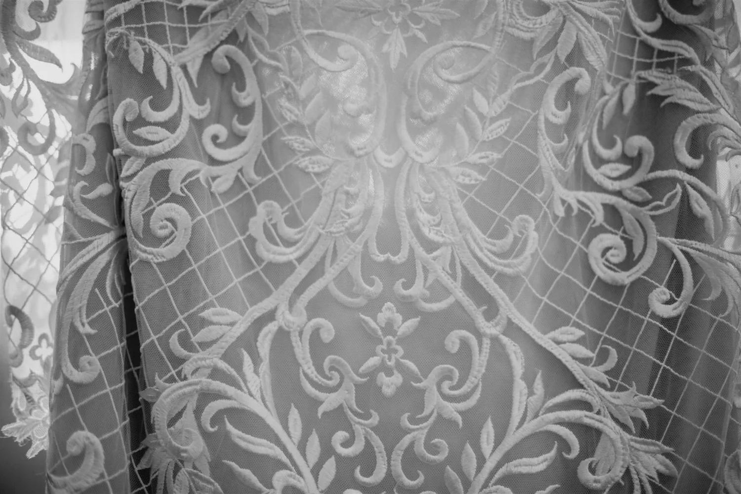 Close-up of a white embroidered lace fabric with intricate floral and scroll patterns.