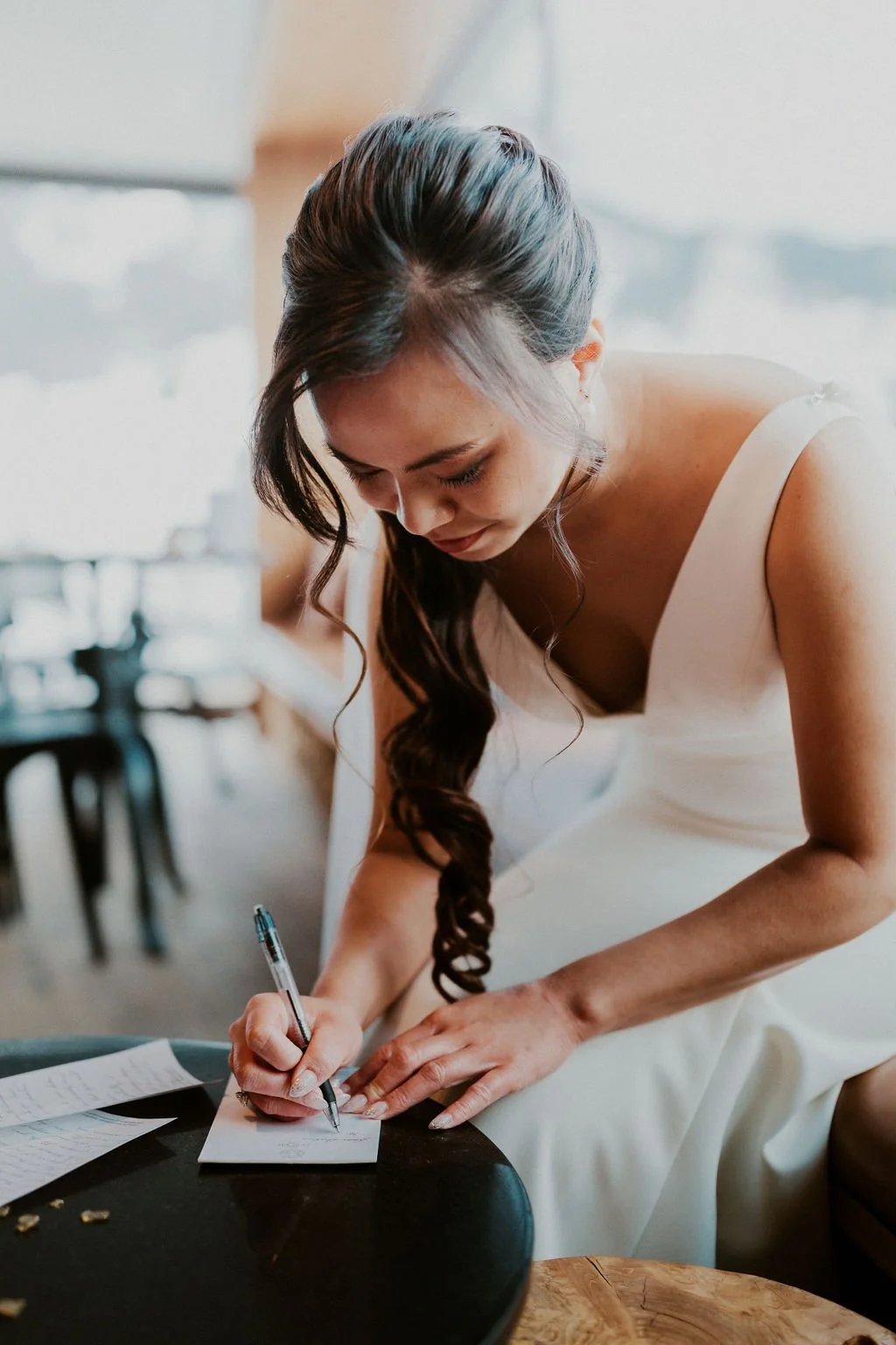 A woman in a white dress is signing a card or note at a table.