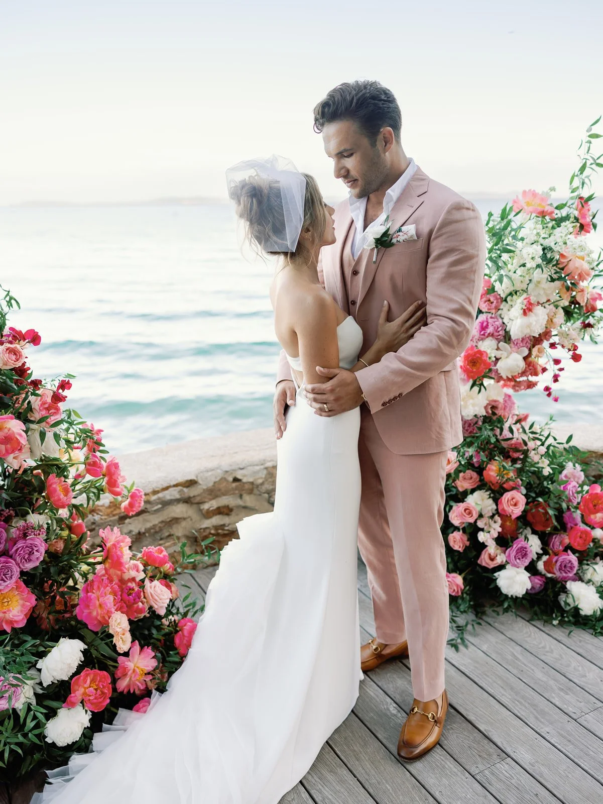 A bride and groom sharing a moment during their seaside wedding, surrounded by colorful flowers, with the ocean in the background.