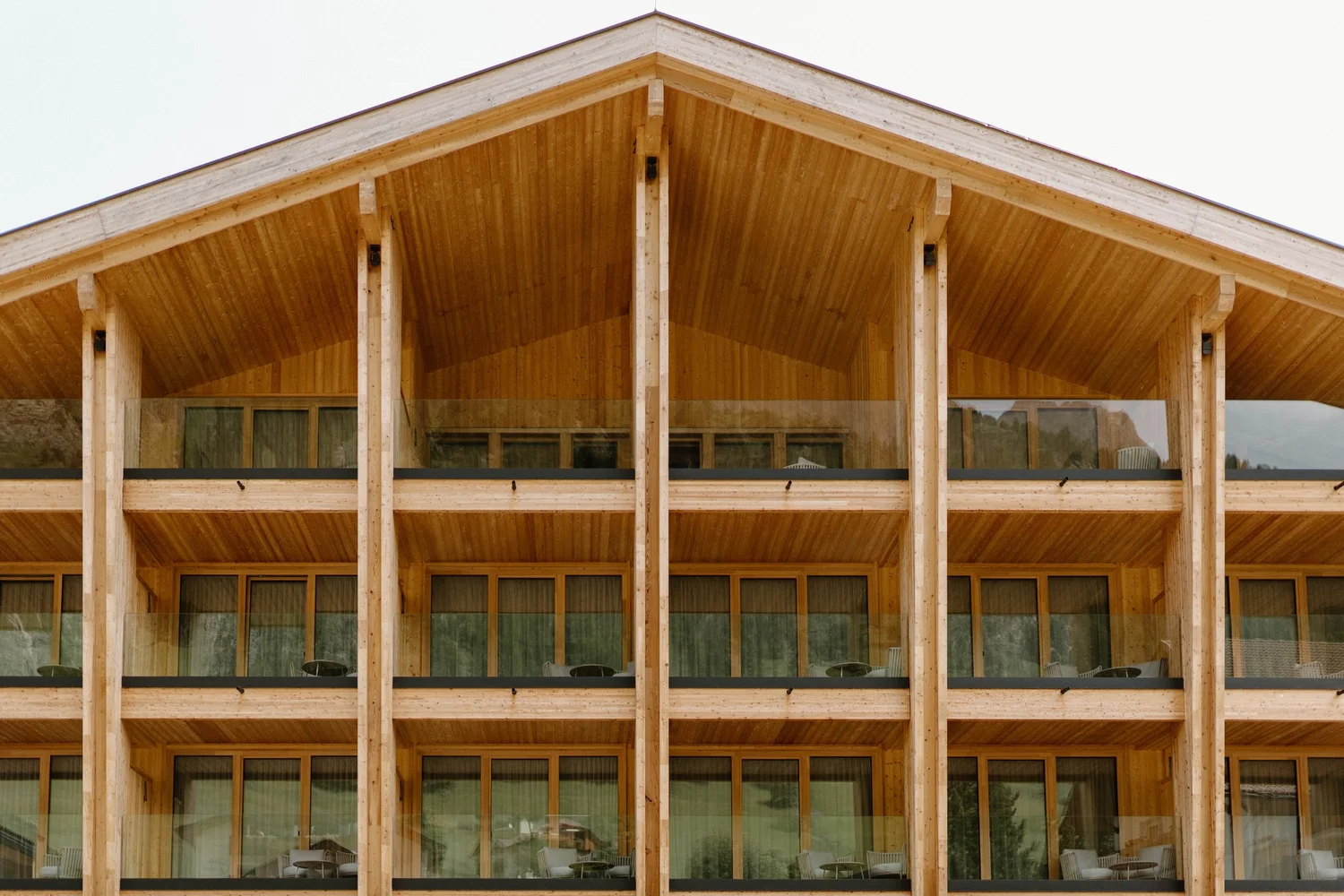 Front view of a multi-story building with a wooden exterior, large glass windows, and a sloped roof.