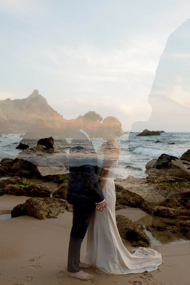 A couple in wedding attire standing on a rocky beach, with the ocean and a rocky island in the background, and a double exposure effect creating a ghostly overlay of a person's face.