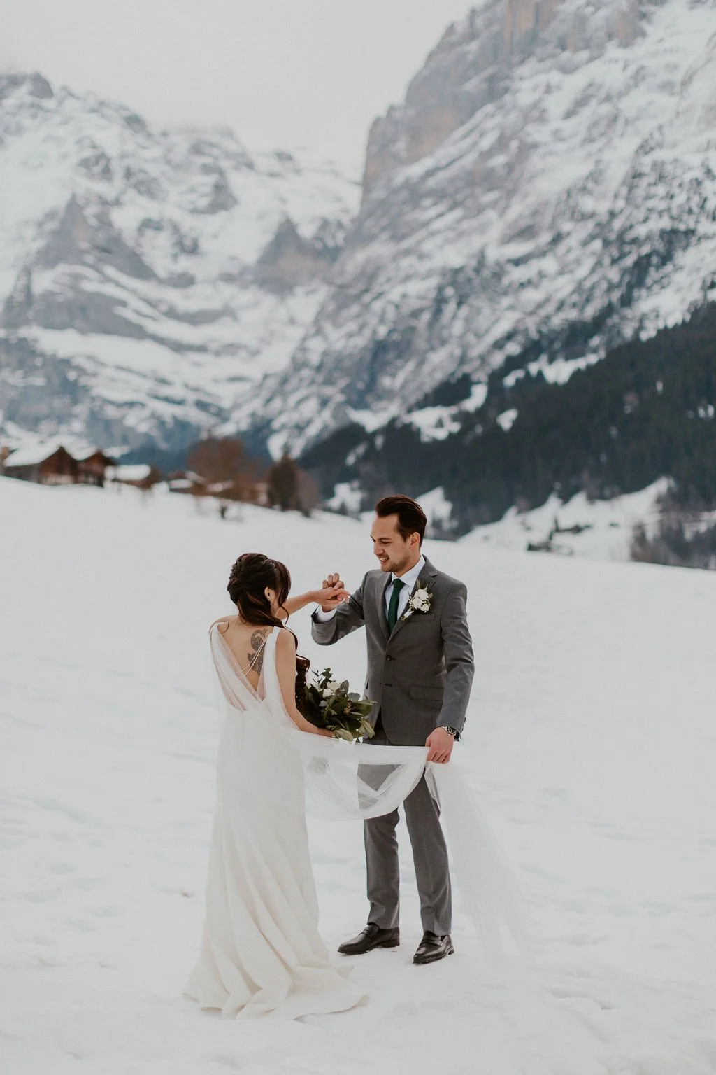 A couple in wedding attire holding hands in a snowy mountain landscape