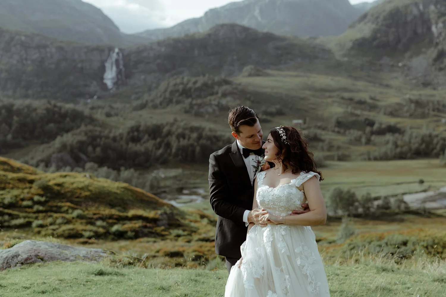 A bride and groom sharing a romantic moment outdoors in a mountainous landscape during their wedding.