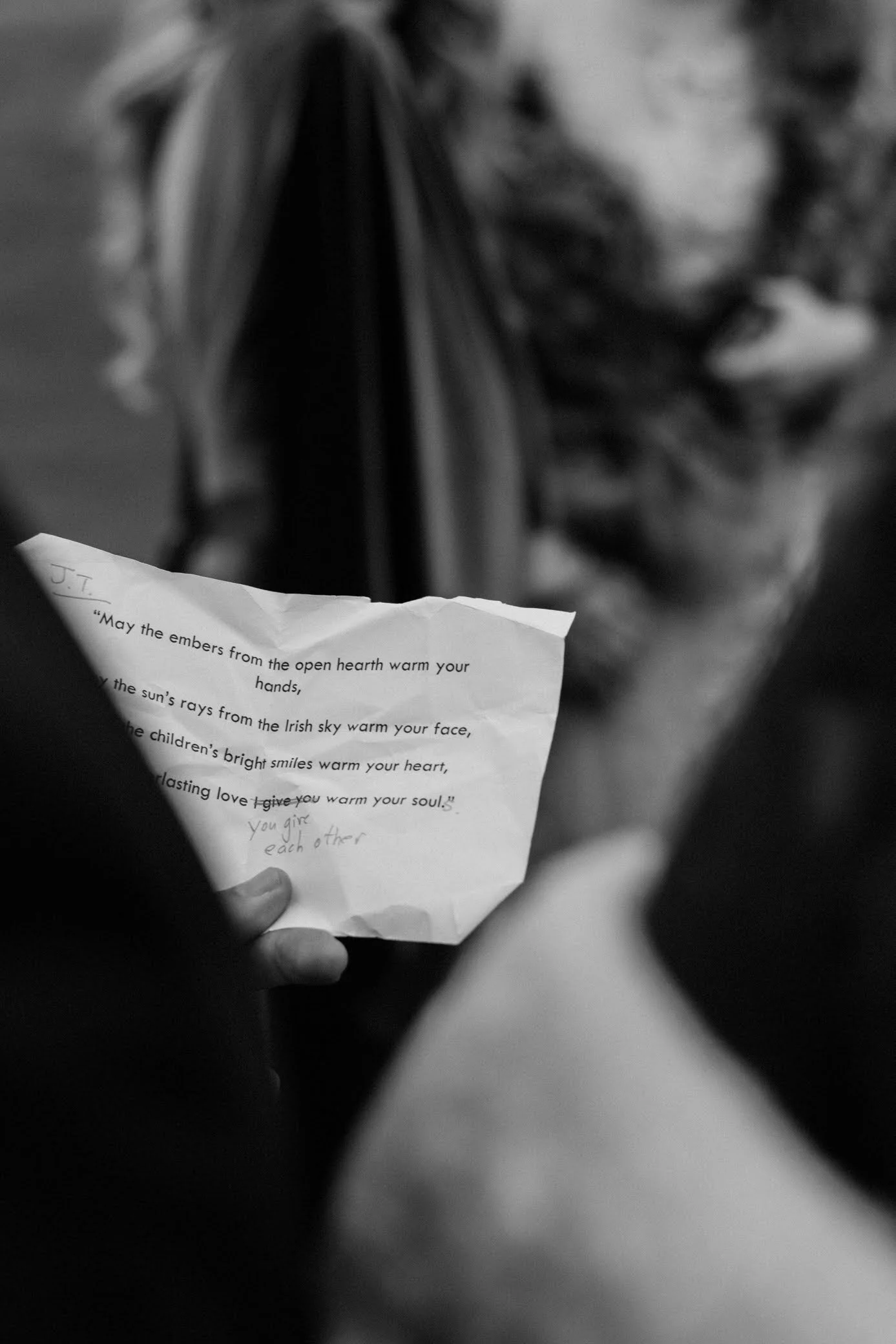 A person holding a crumpled piece of paper with a poem printed on it, in a blurry black-and-white photograph.