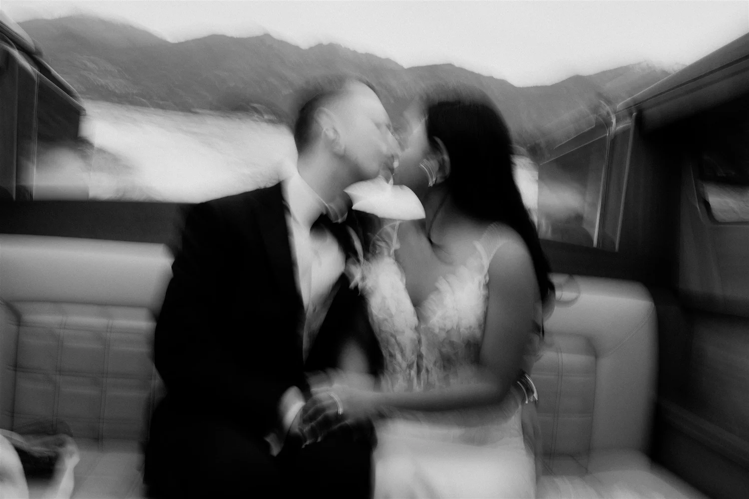 A black-and-white photo of a couple kissing inside a vehicle, with mountains visible through the window behind them.