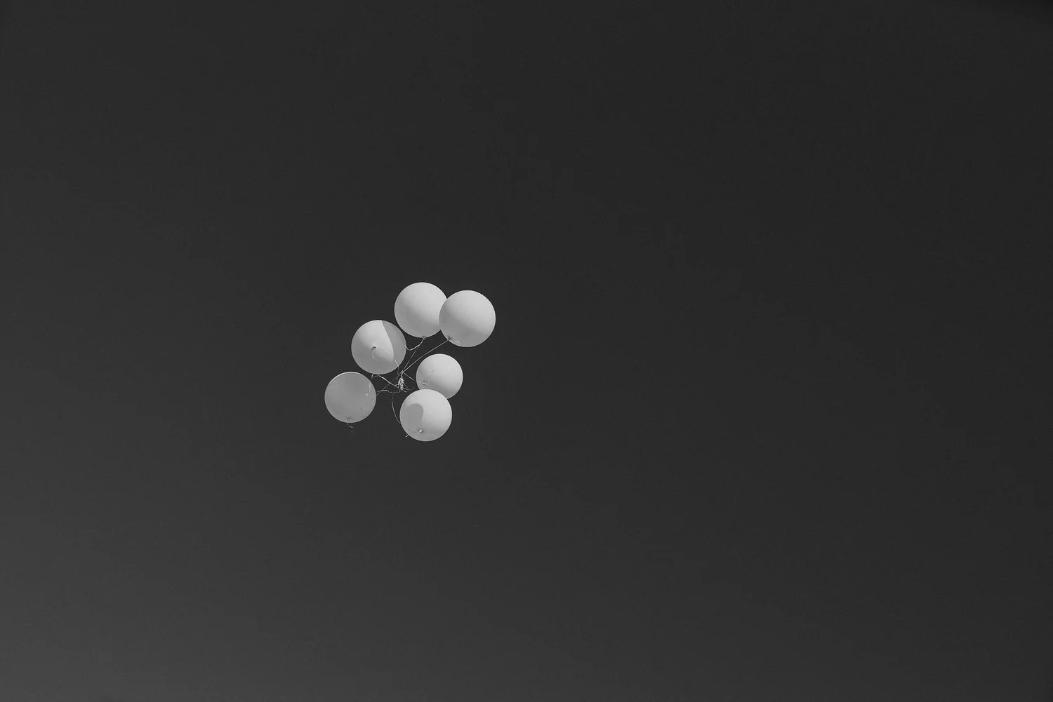 A bunch of white balloons floating against a dark, cloudy sky.