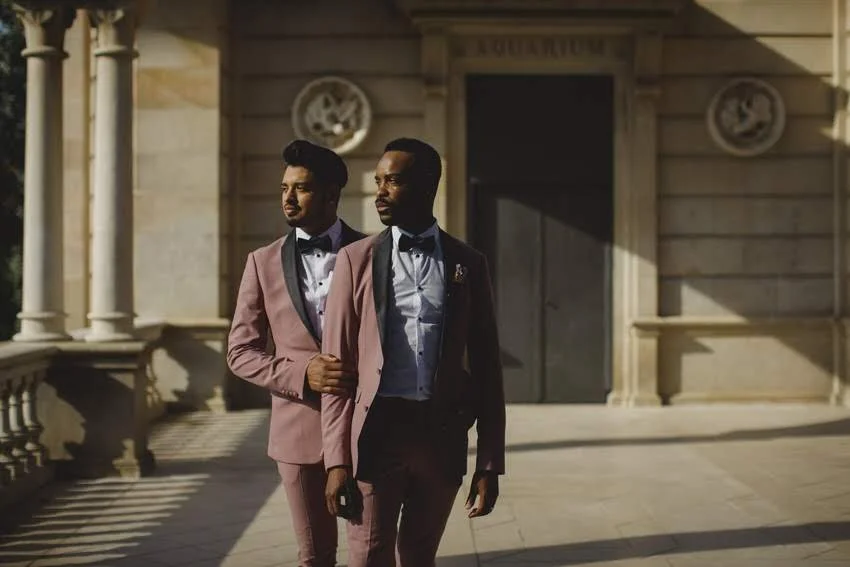 Two men in suits walking outside of a building with classical columns and decorative medallions, possibly courthouse or government building.