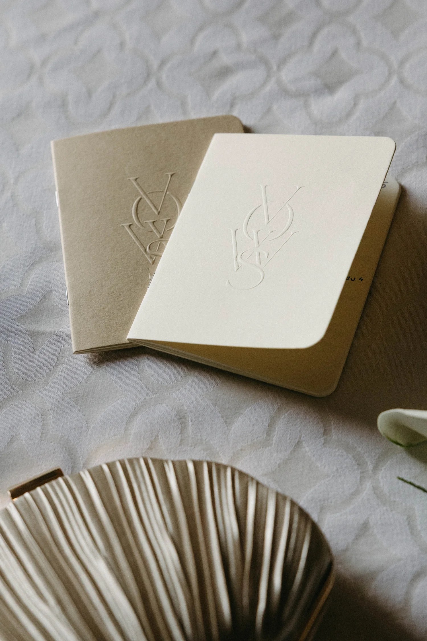 Close-up of an open book or booklet with embossed letter V on its cover, placed on a textured white surface.