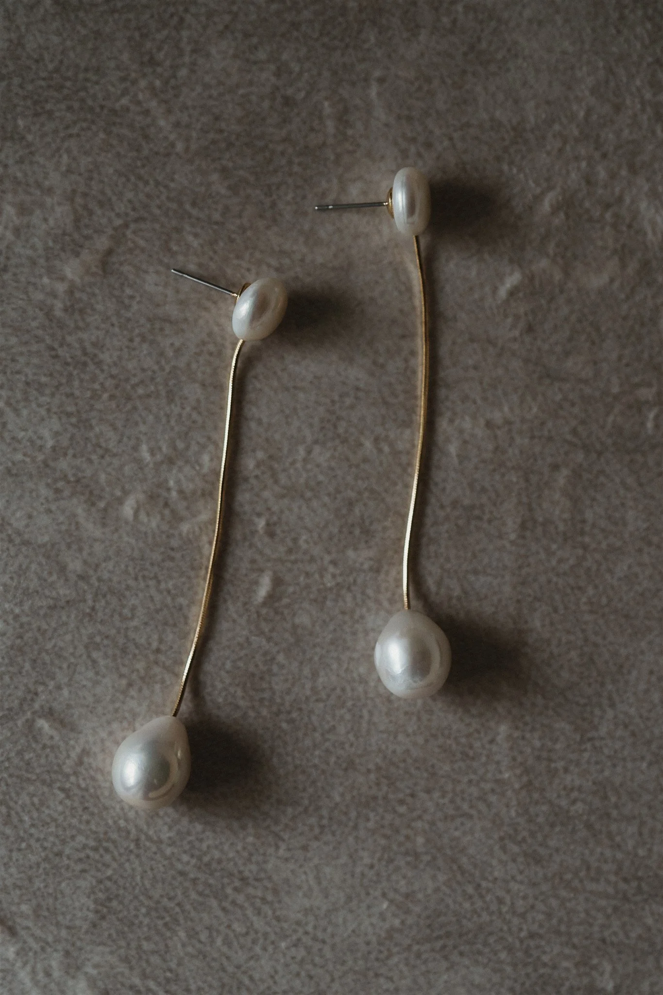 Close-up of pearl earrings with gold hooks on a beige textured background.