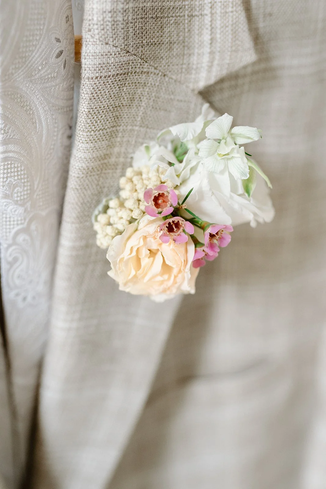 Close-up of a cream-colored flower and small pink blooms attached to a textured beige fabric with lace and embroidery details.