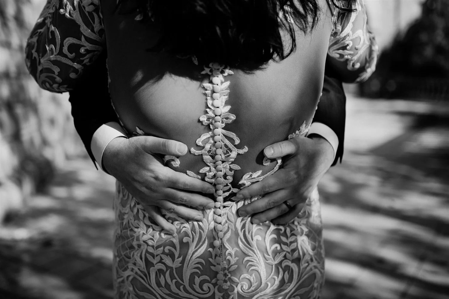 Black and white photo of a person wearing a dress with intricate embroidery and buttons, holding their stomach with both hands.