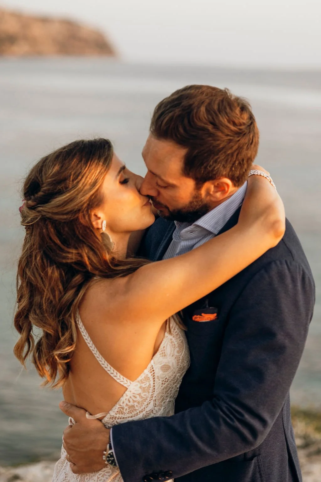 A couple kissing on a beach at sunset, embracing each other closely.