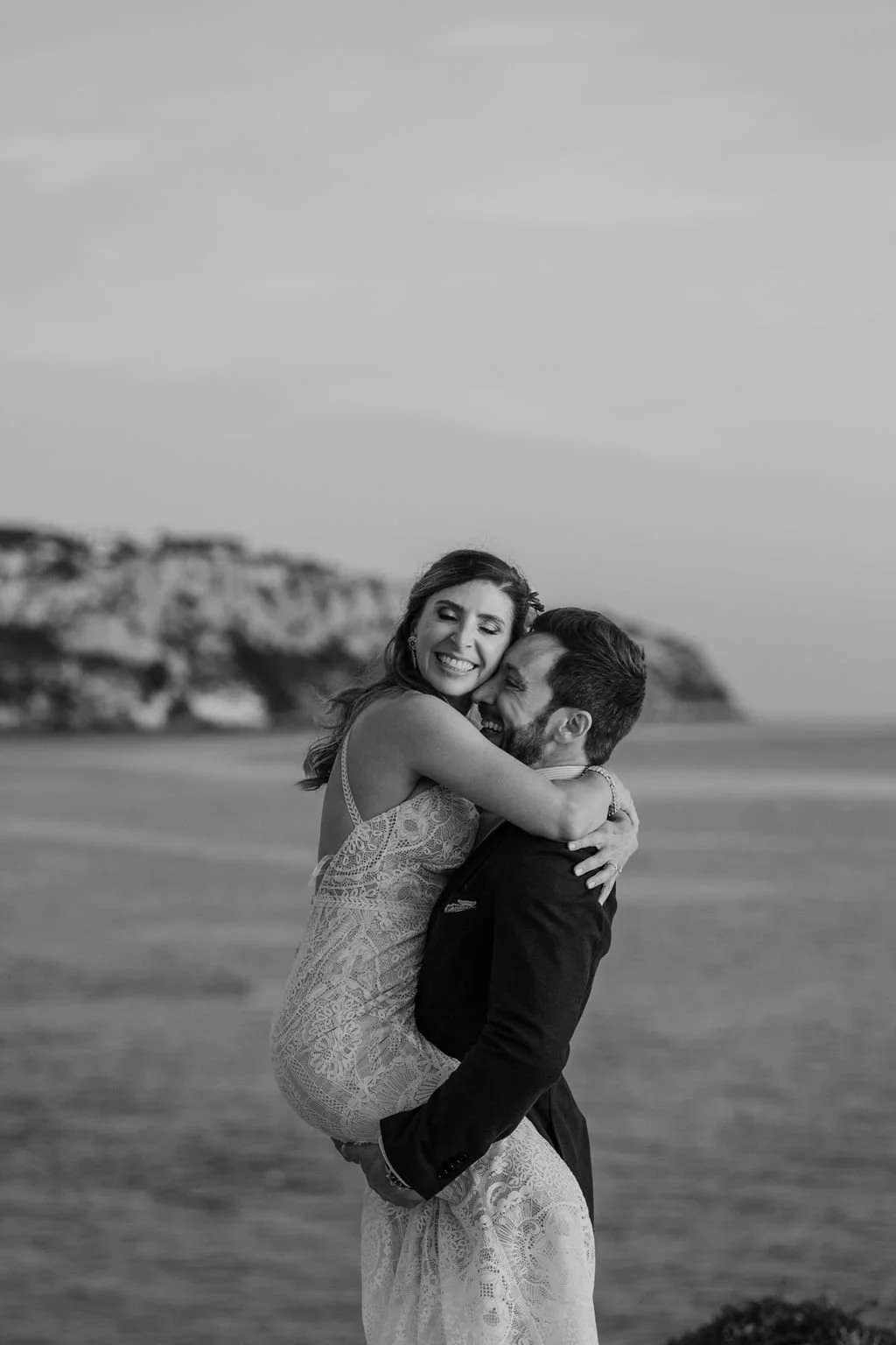 A happy couple hugging on a beach, with cliffs in the background, black and white photo.