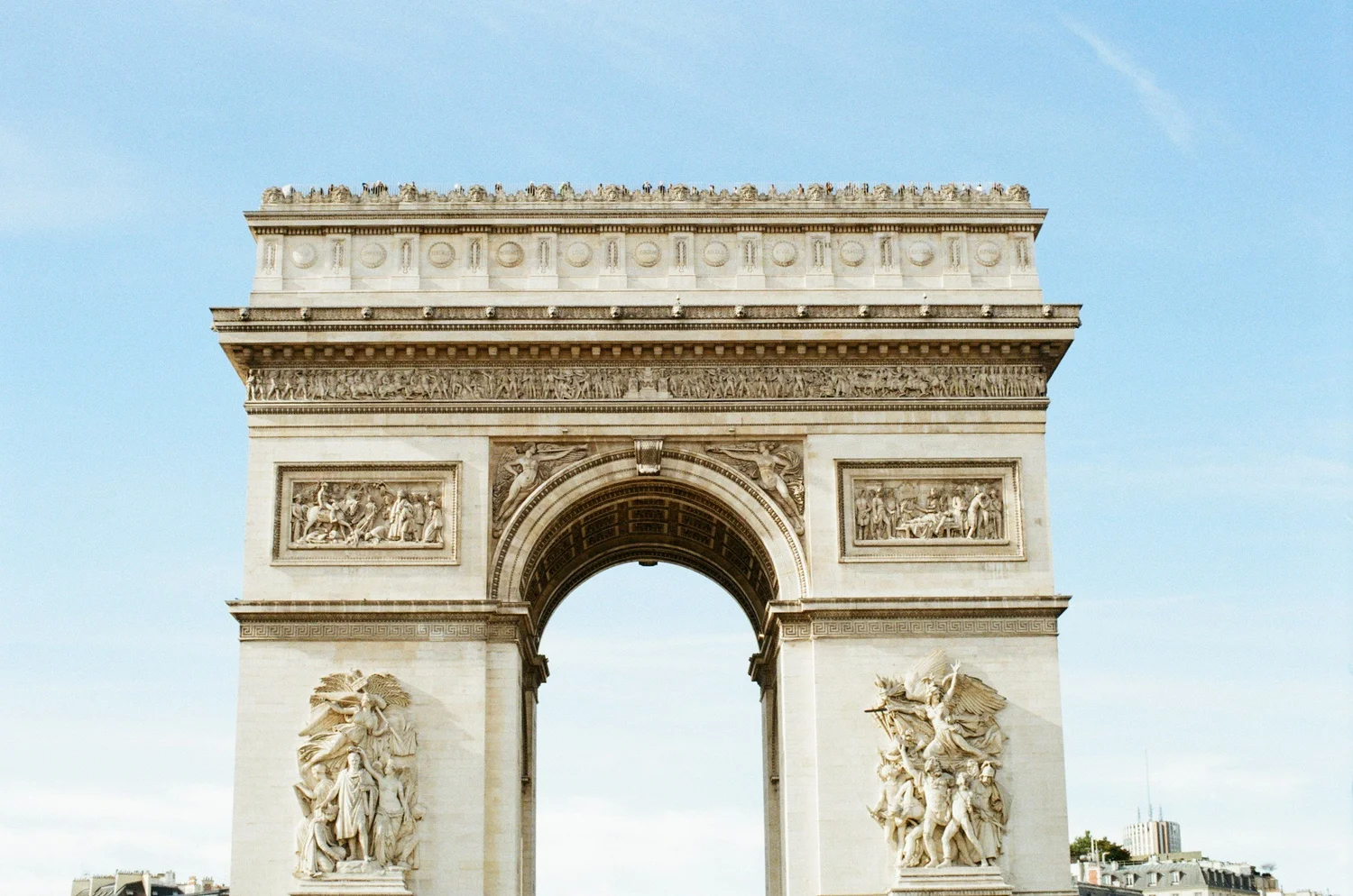 Close-up of the Arc de Triomphe, a Paris monument, showing detailed sculptures and carvings on the arches against a light blue sky.