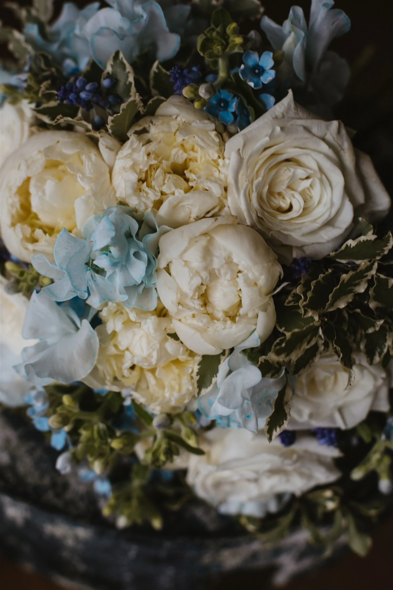 Close-up of white roses, blue hydrangeas, and small blue flowers in a floral arrangement.