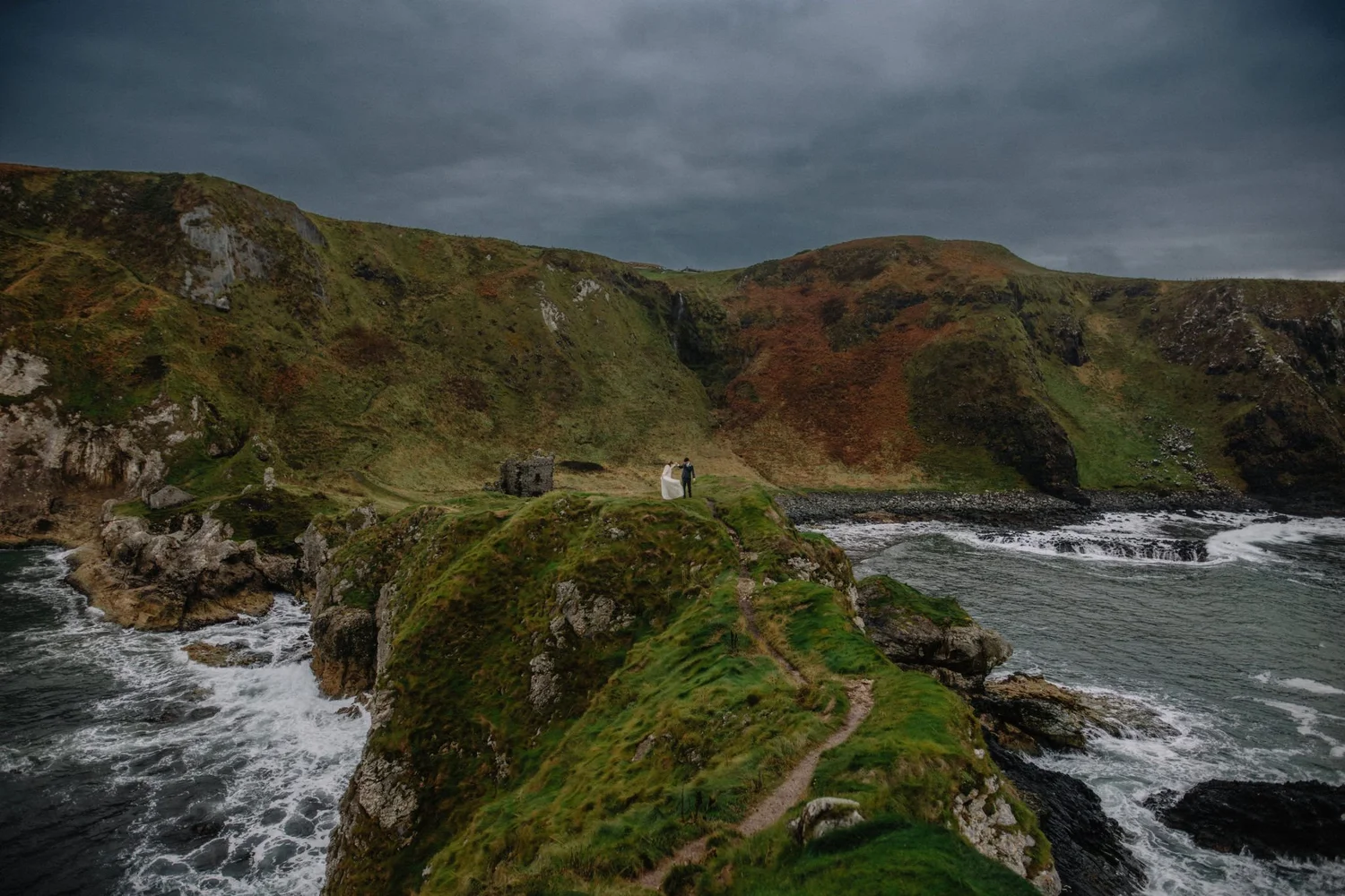 A shipwreck on a grassy hillside near the water under a dark cloudy sky.