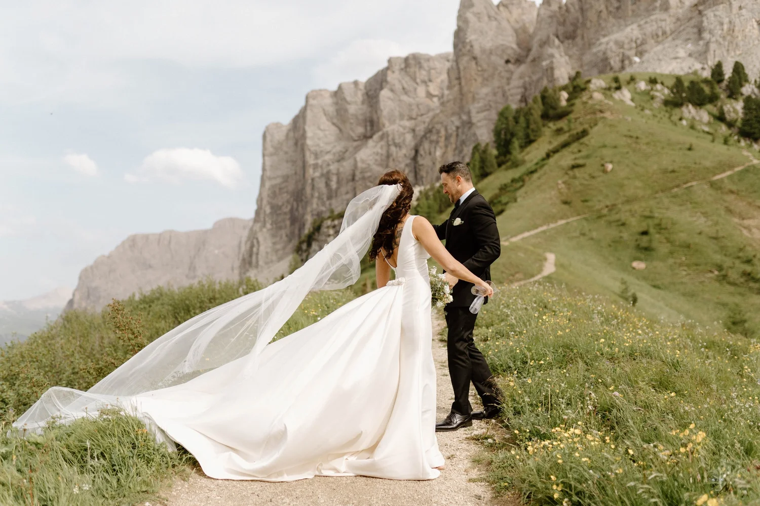 A bride and groom in wedding attire sharing a moment in an outdoor mountainous setting.