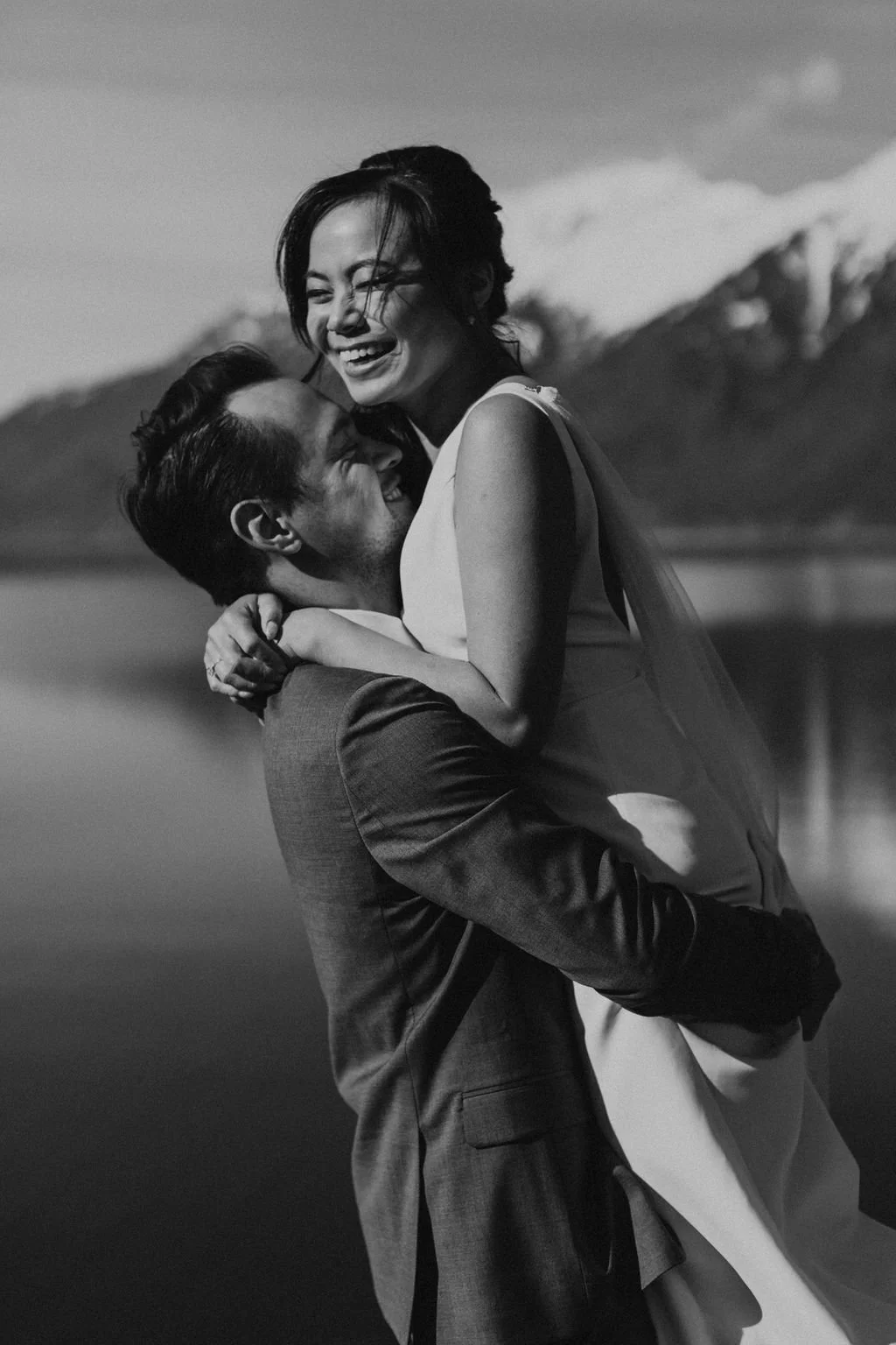 A happy couple enjoying a moment together outdoors, with mountains and a lake in the background, black and white photograph.