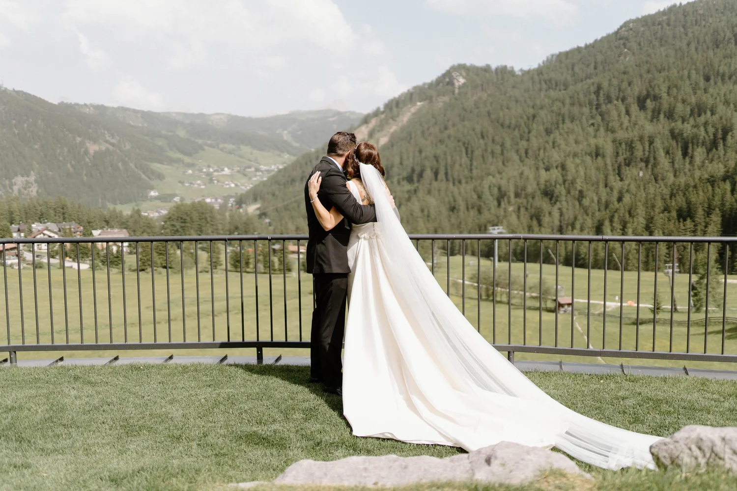 A bride and groom embracing on a balcony with a mountain landscape in the background.