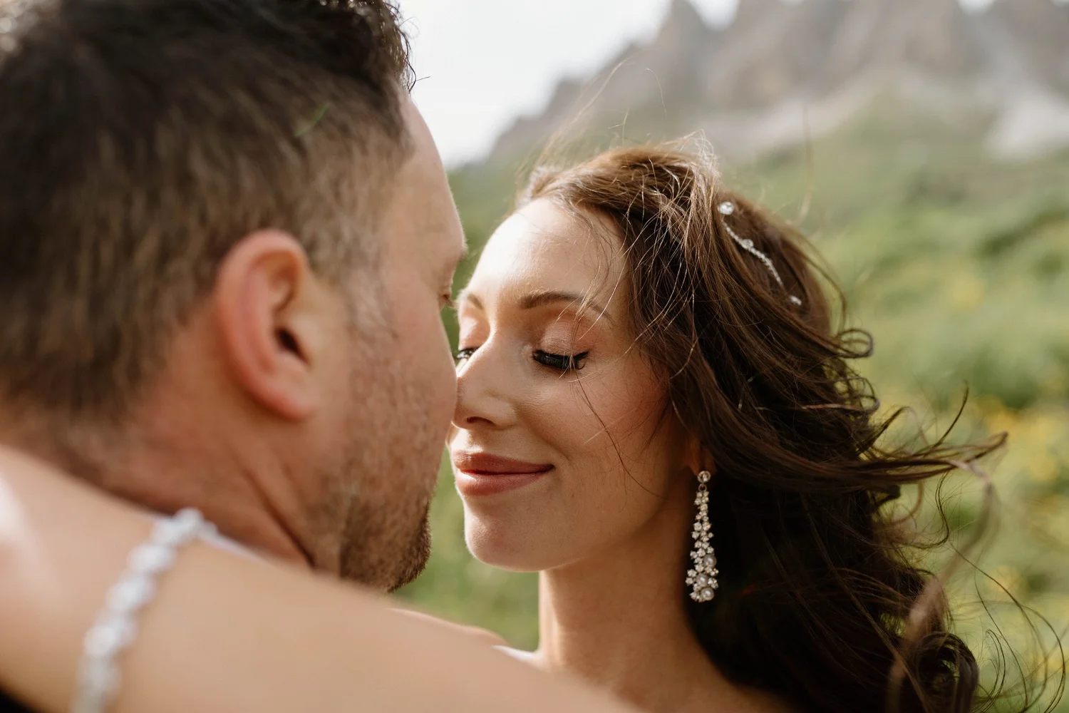 A close-up of a bride and groom about to kiss outdoors, with blurred greenery in the background.