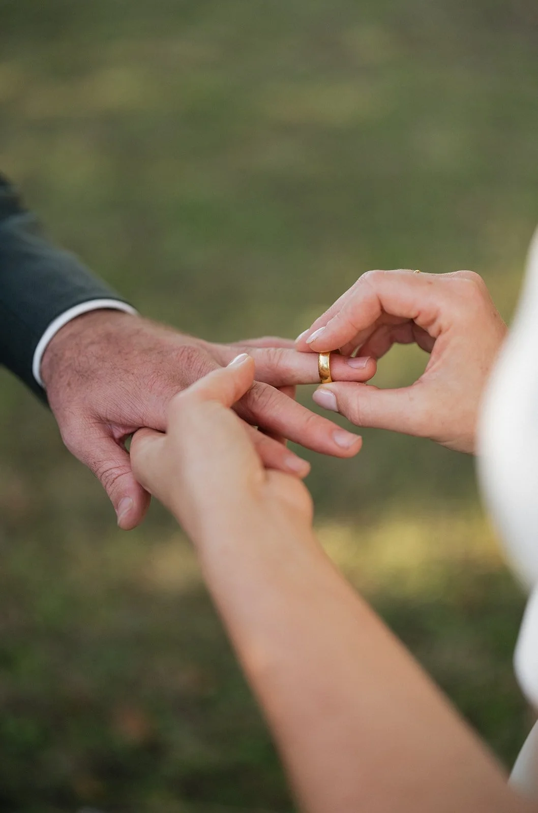 A person wearing a wedding ring is placing it on the finger of another person, during a wedding or engagement ceremony.