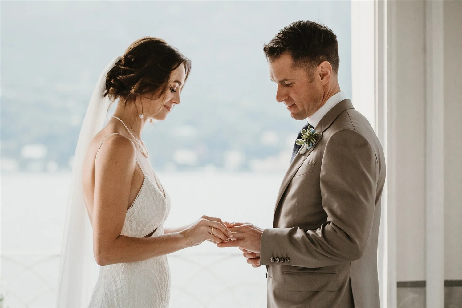 Wedding couple holding hands during vows in front of a large window with a city view.