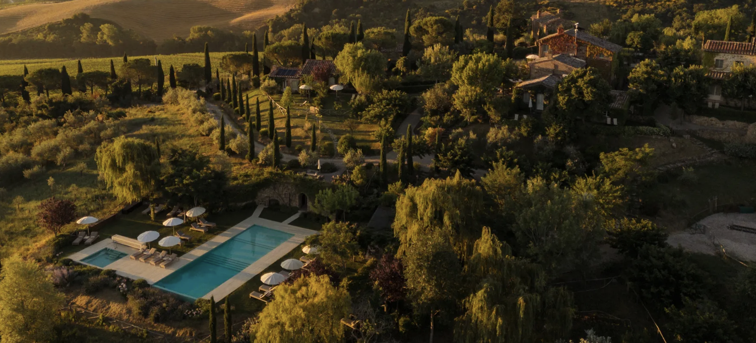 Aerial view of a countryside estate with a swimming pool, surrounded by trees and hills, during golden hour.