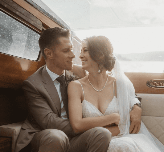 A newlywed couple sitting close together inside a boat, smiling and looking at each other.
