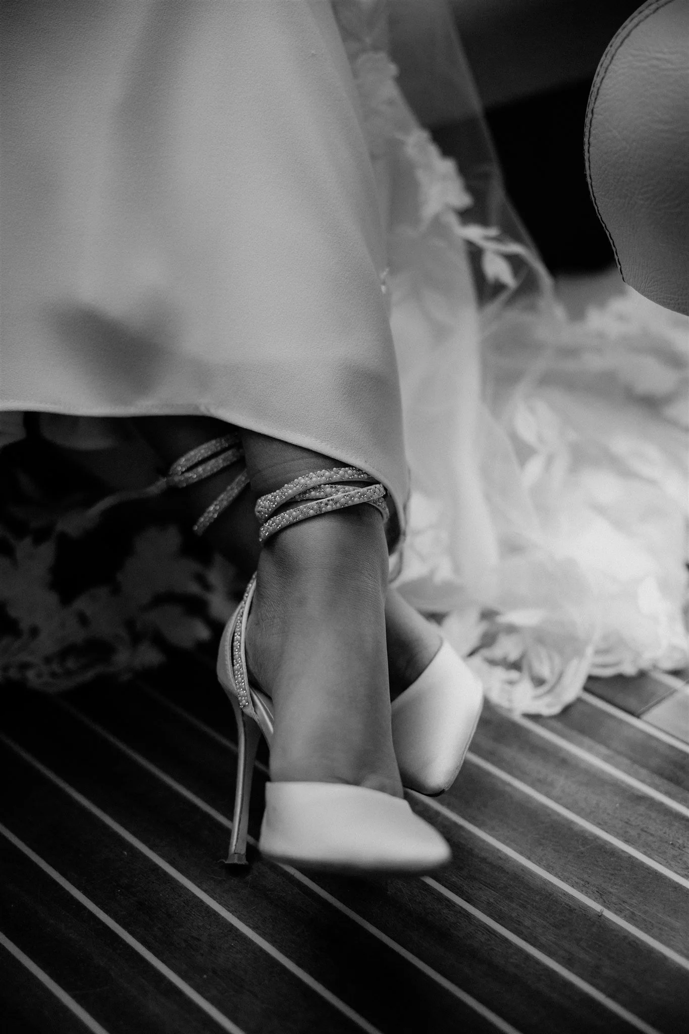 A close-up of a person's legs and feet, showing stylish high-heeled shoes with straps and a glittery finish, on a striped carpet. The person is also wearing an elegant dress and jewelry.