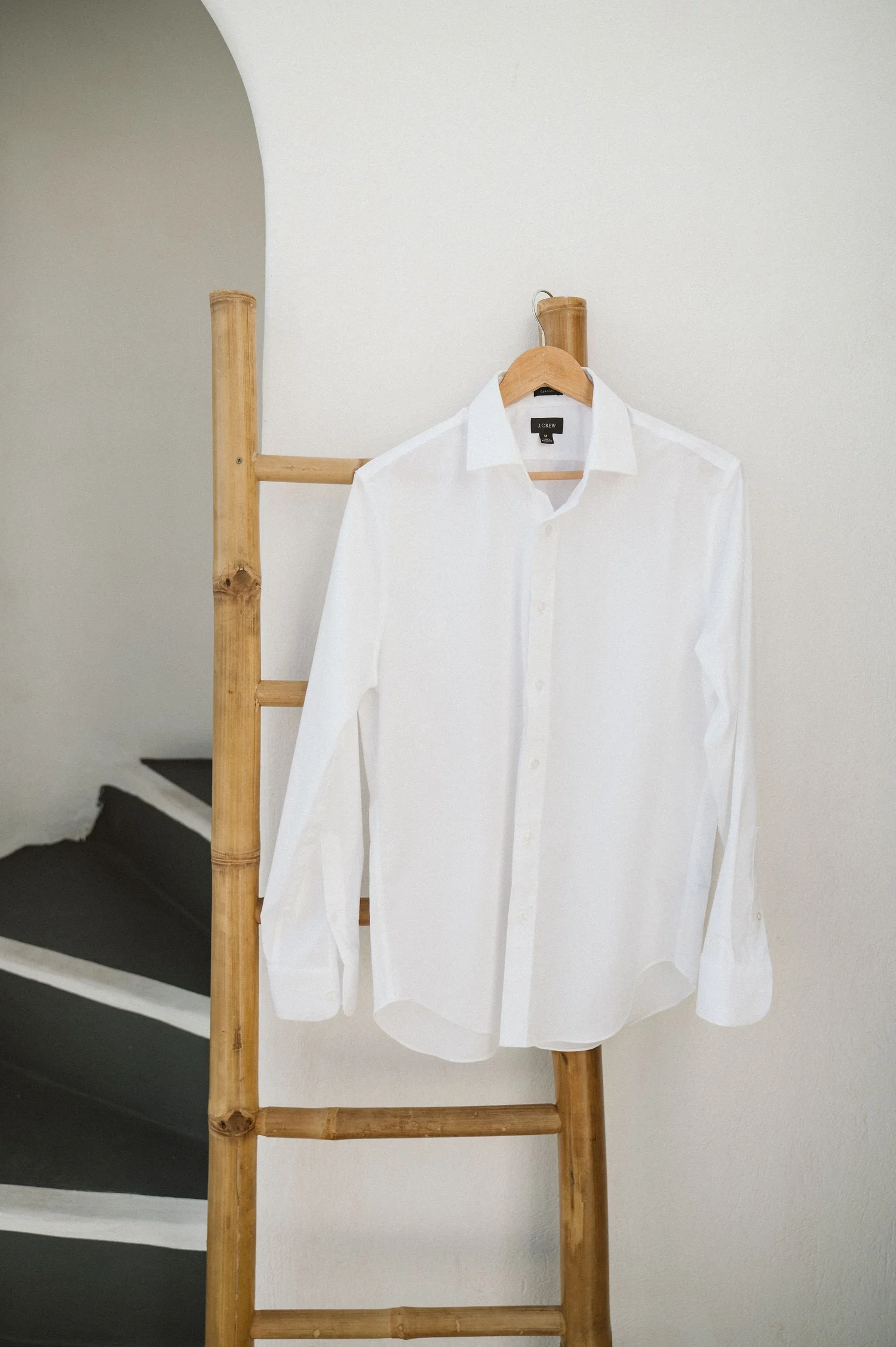 A white button-up shirt hanging on a wooden ladder against a plain white wall.