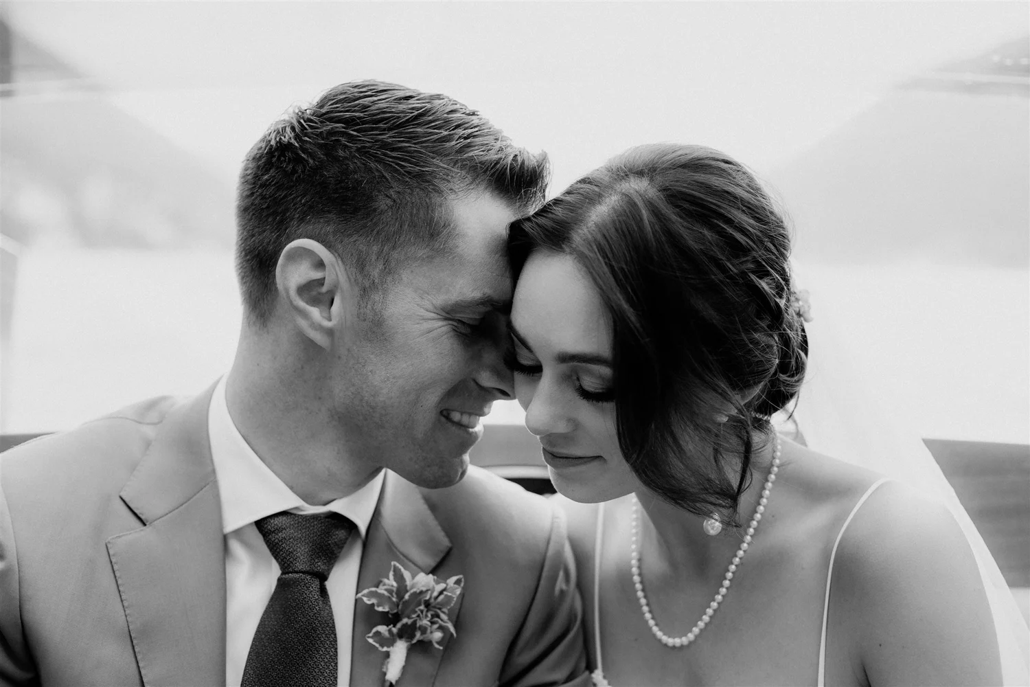 Black and white photo of a smiling couple with foreheads touching, dressed in wedding attire, suggesting an intimate moment during their wedding.